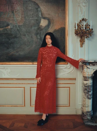 An elegant, full-length portrait of an Asian woman in a red lace dress, standing in front of a vintage painting in an ornate interior.
