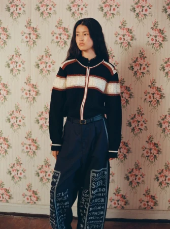 Model wearing a black patterned zip cardigan and trousers against a floral wallpaper background for the Sea RS26 Editorial.