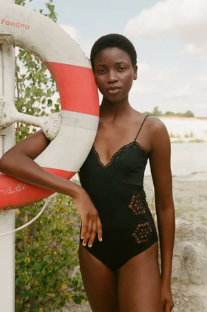 Model in black swimsuit leaning against a red and white lifebuoy ring outdoors