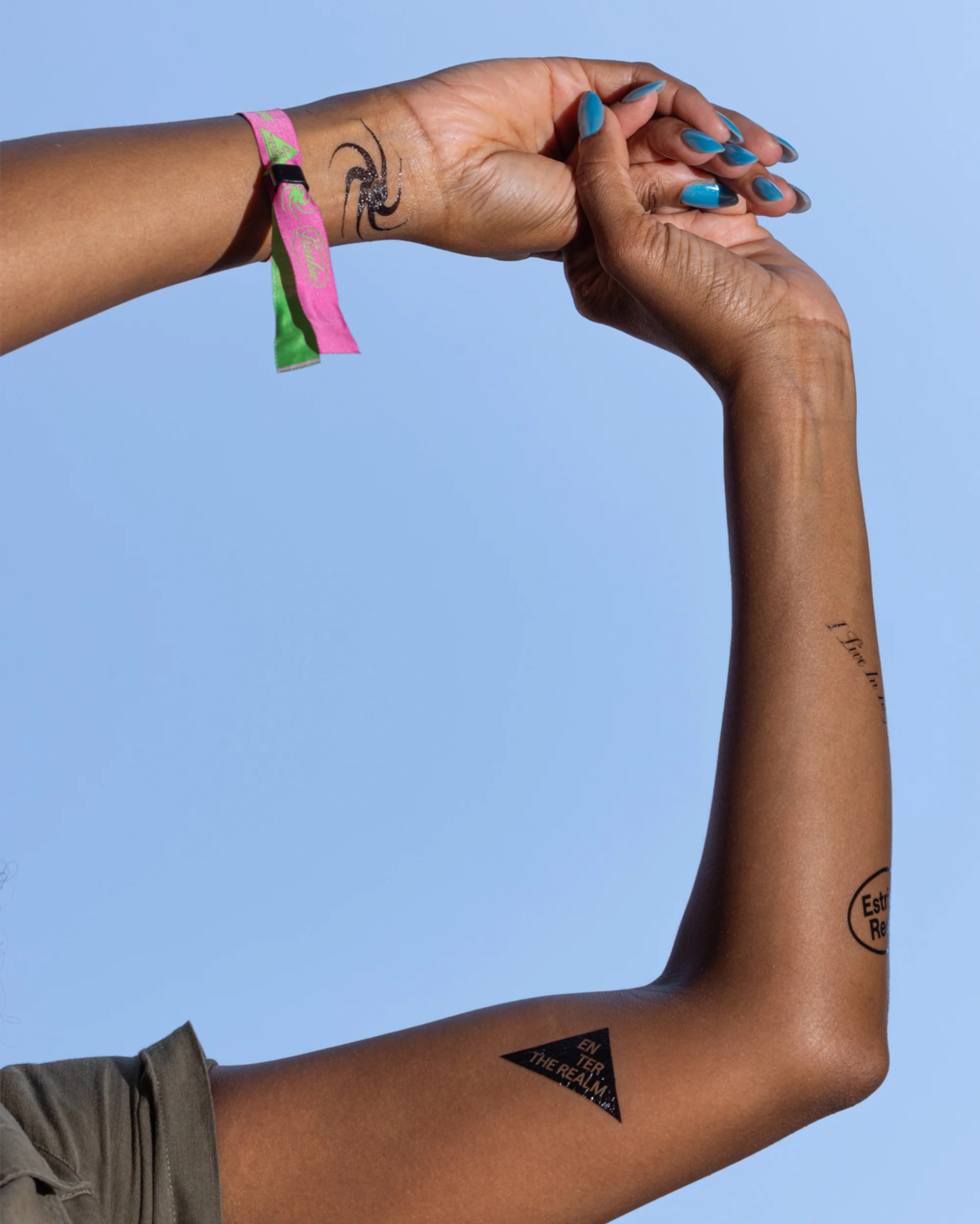 Woman with dark skin poses her arm and hand with tattoos against a bright blue sky, creating a visually striking composition.