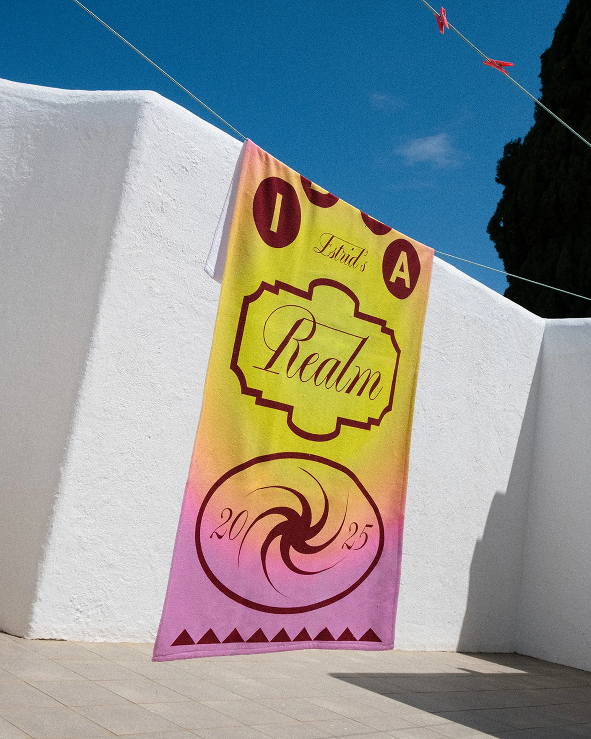 Outdoor shot of a colorful patterned beach towel hanging on a clothesline against a white wall and blue sky backdrop on a sunny day.