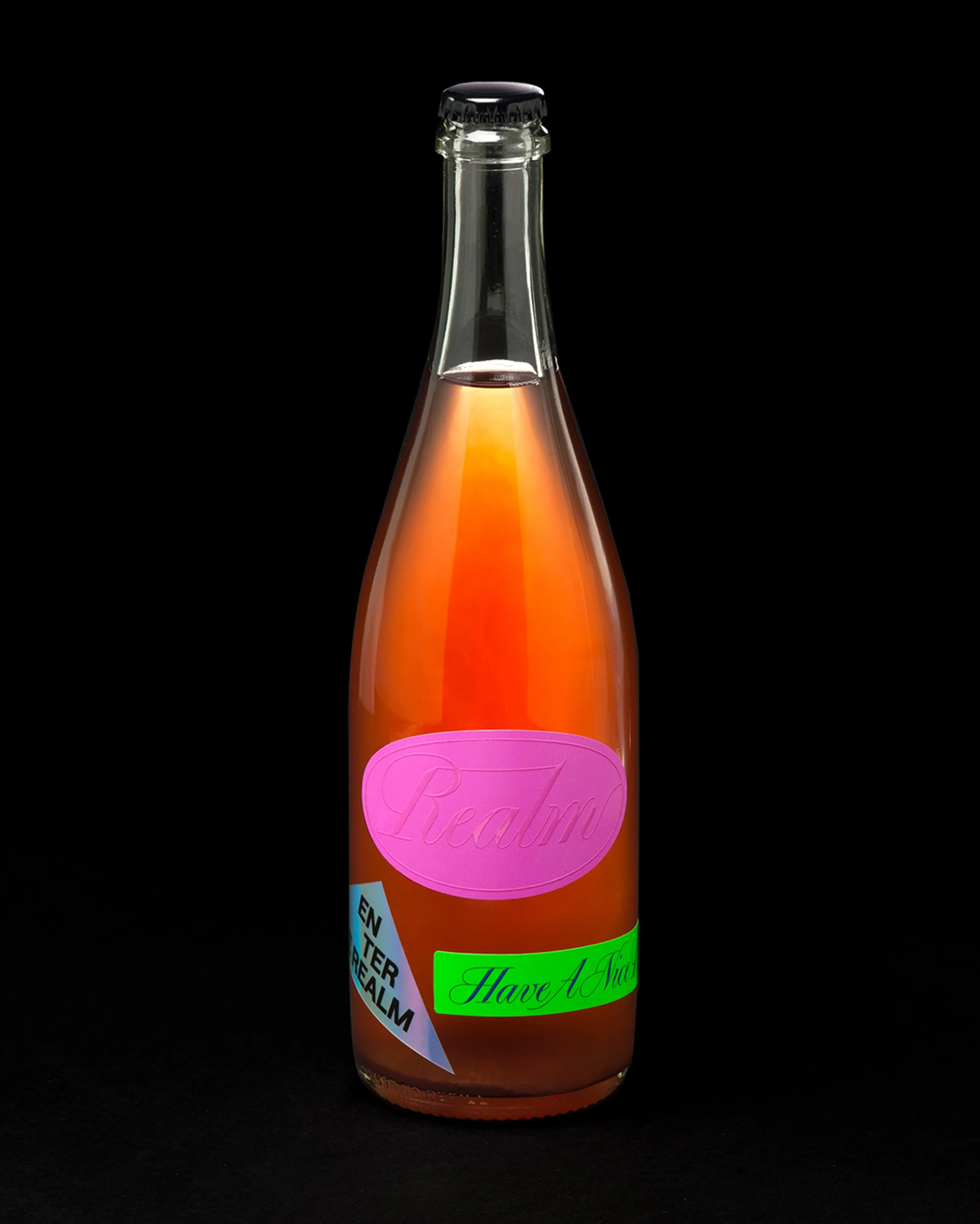 Close-up studio shot of a glass bottle filled with pink liquid, adorned with pink and green labels, set against a dark background.