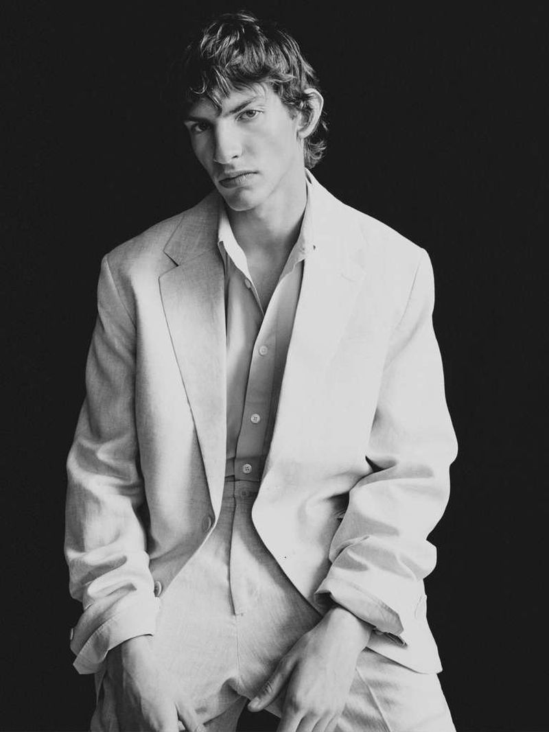 Monochrome portrait of an adult male wearing a light-colored suit in front of a dark background with soft, diffused lighting.