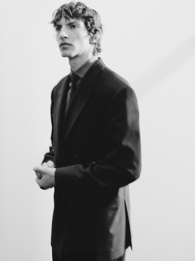 A young male model in a dark suit jacket posing against a plain neutral background for Zara Man.