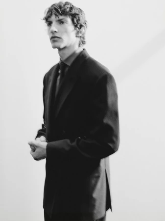 A young male model in a dark suit jacket posing against a plain neutral background for Zara Man.