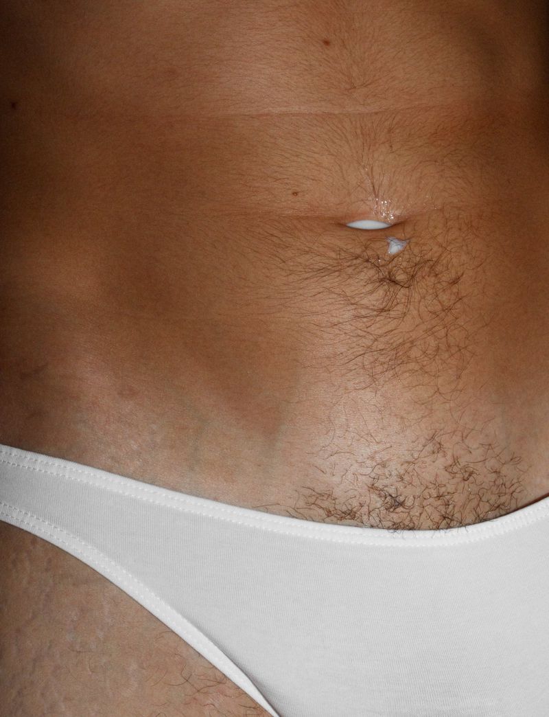 Close-up shot of a person's midsection with tan skin, a navel with a white substance, and white underwear visible at the lower abdomen.