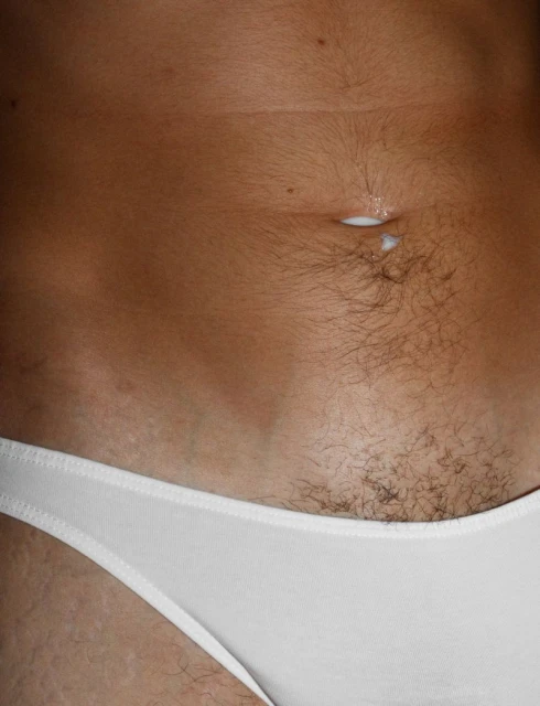 Close-up shot of a person's midsection with tan skin, a navel with a white substance, and white underwear visible at the lower abdomen.