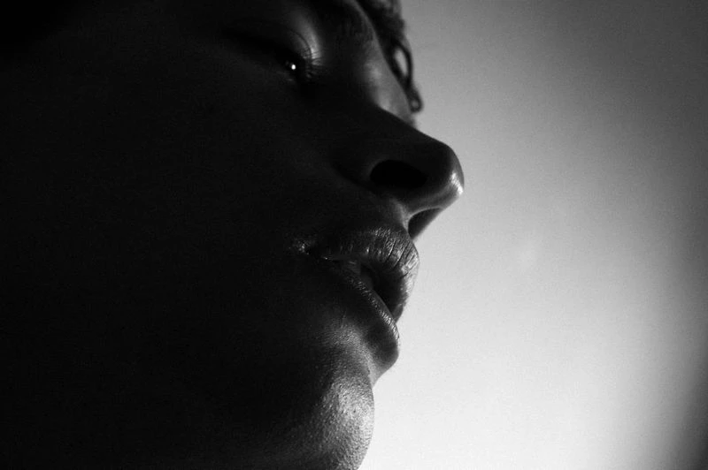 Monochromatic portrait of a person with head in profile, featuring a nose, lips, and eyelashes against a light grey background.