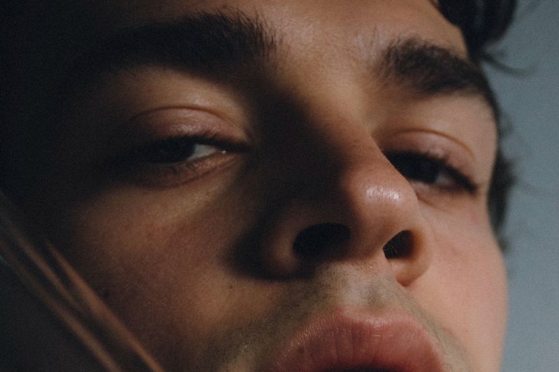 Extreme close-up shot of a young adult male's face showing his eye, nose, and lips. Focus on facial details, skin texture, and lighting.