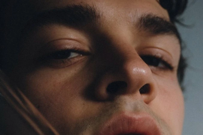 Extreme close-up shot of a young adult male's face showing his eye, nose, and lips. Focus on facial details, skin texture, and lighting.