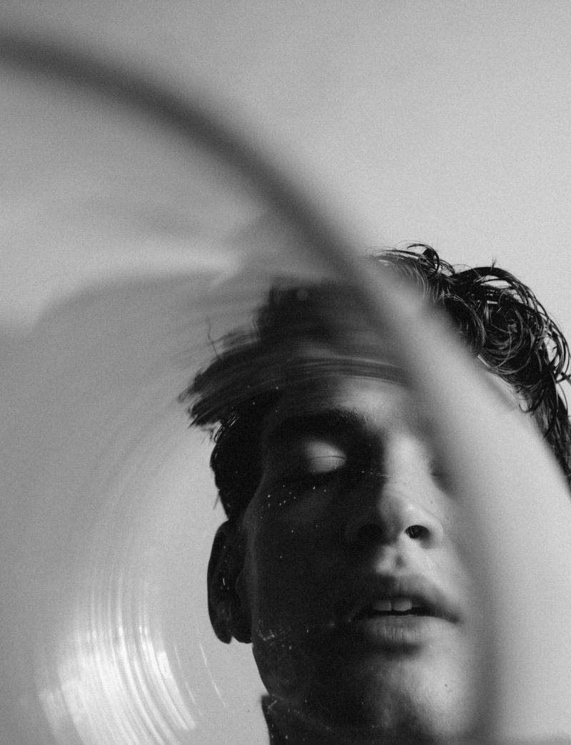 Monochrome portrait of an adult with eyes closed, visible from the shoulders up, and a blurred circular design superimposed.
