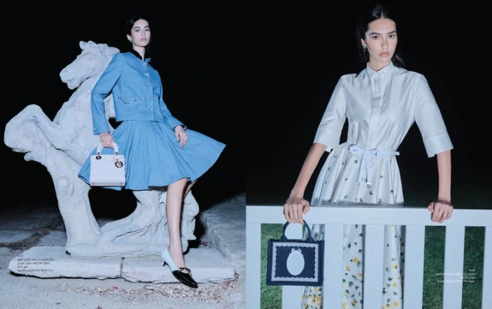 Two women pose with designer handbags in a dark outdoor fashion editorial. One woman poses with a horse statue; the other, with a fence.