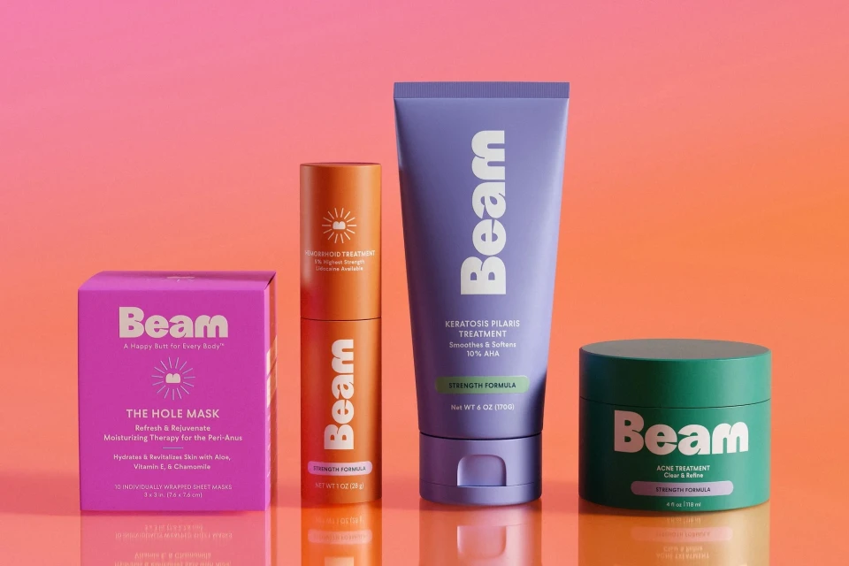 Four Beam brand skincare products including a face mask, acne treatment, and keratosis pilaris treatment arranged against an orange background.