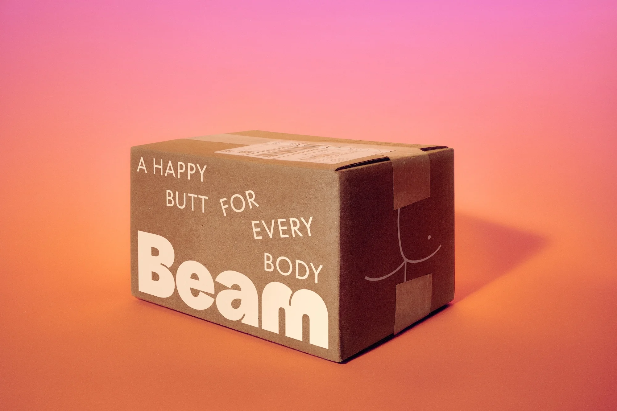 Brown cardboard box with white text 'A happy butt for every body' and a cheeky illustration, against a vibrant orange-to-pink gradient.