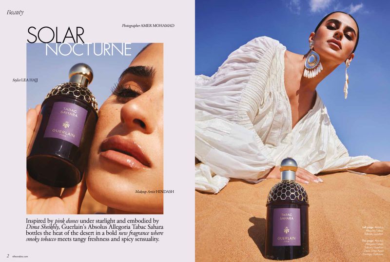 Beauty editorial shot featuring a fair-skinned female model in a white dress, with a Guerlain perfume bottle in the desert under a clear blue sky.