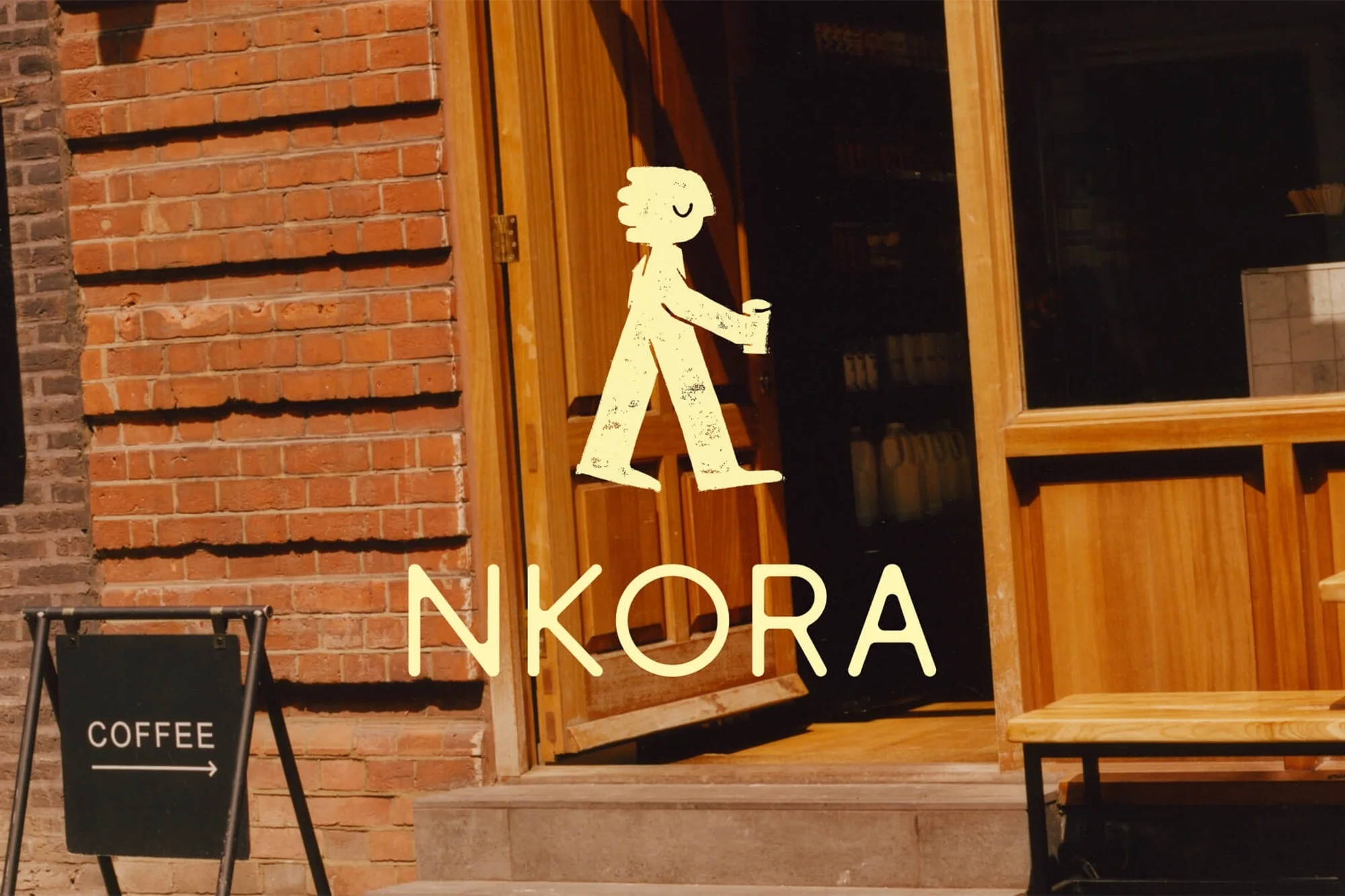 Illustration of a person holding a cup on wooden doors with a brick wall and a coffee sign in front of the 'Nkora' cafe.