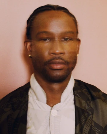 Portrait of Akinola Davies Jr in a patterned jacket and white shirt against a neutral background for Wonderland Magazine