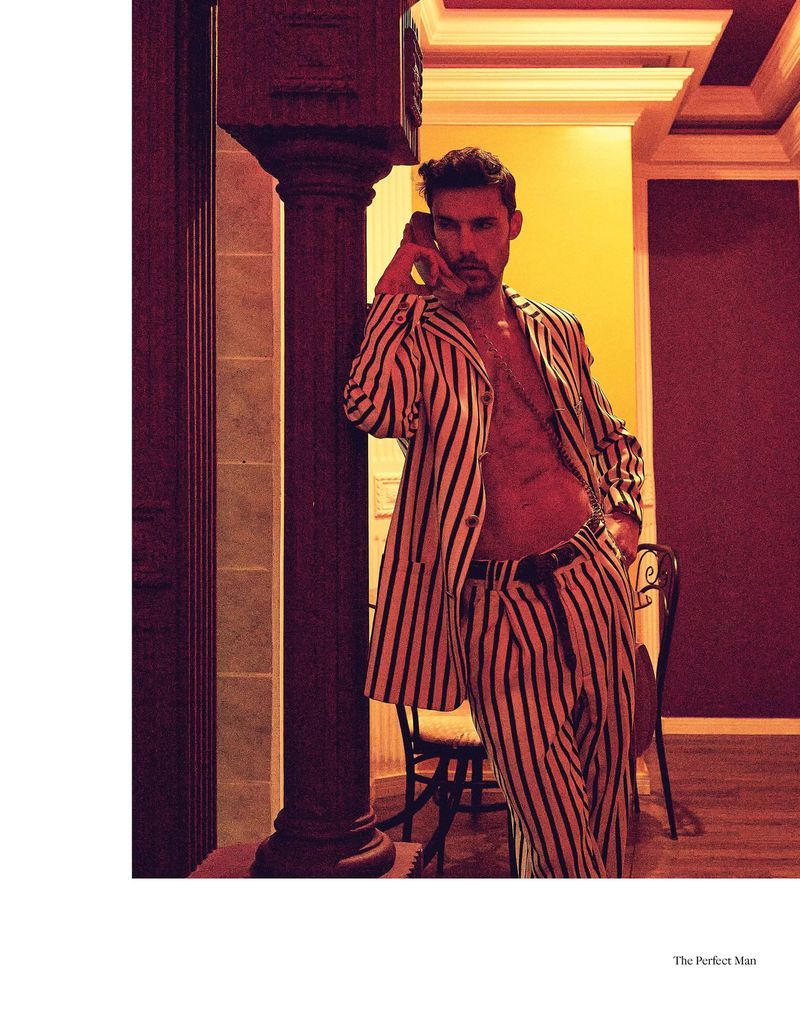 Man in a striped suit leans against a column talking on an old telephone, warm lighting, interior setting, fashion photography.