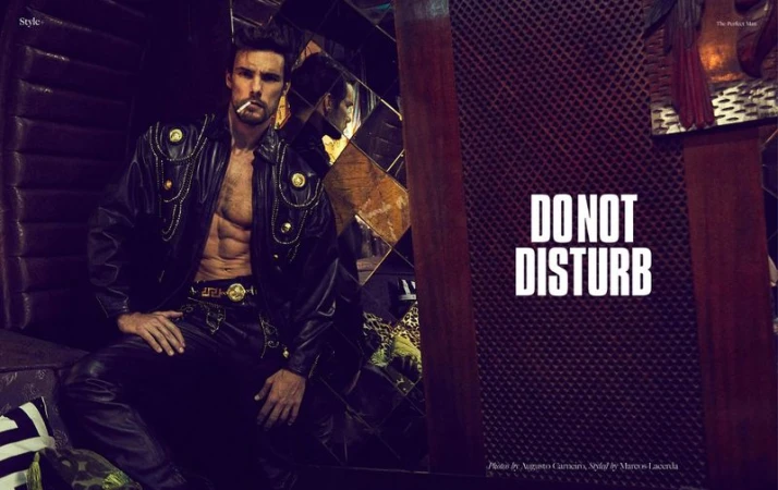 Model Ismael Werlang seated in a black leather jacket with gold hardware, holding a cigarette for The Perfect Man Magazine.