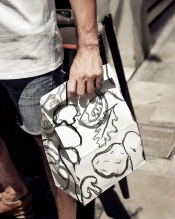 Man holding a patterned paper bag wearing a white t-shirt and denim shorts