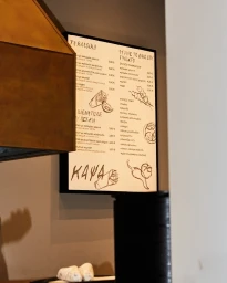 Close-up interior view of a framed menu sign with handwritten Greek typography and sketches mounted on a wall for Kapsa.
