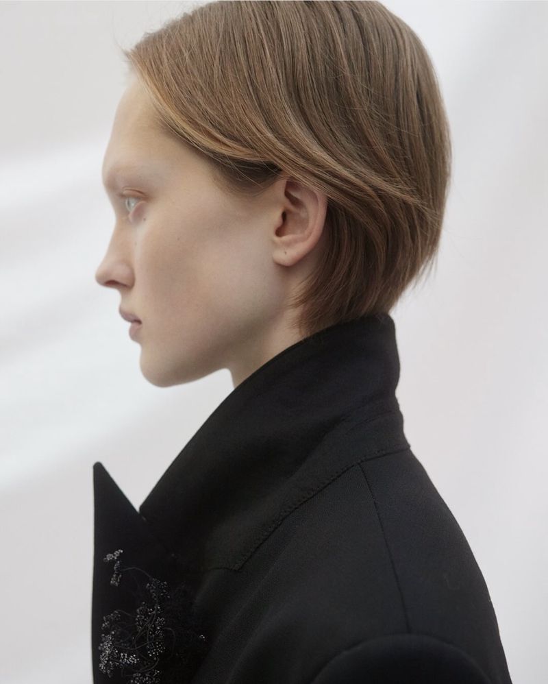 Profile shot of a fair-skinned young adult female with short brown hair wearing a black jacket against a white backdrop.