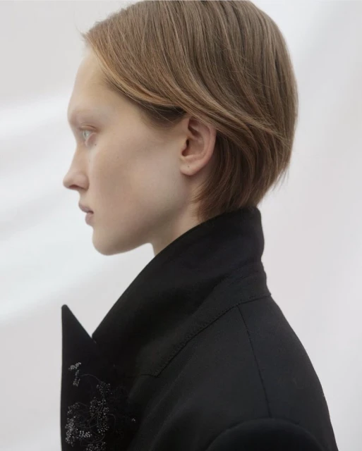 Profile shot of a fair-skinned young adult female with short brown hair wearing a black jacket against a white backdrop.