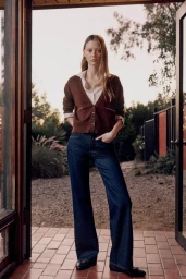 Model standing outdoors on a brick patio wearing a brown cardigan and denim jeans for Everlane
