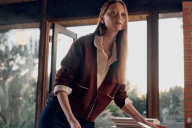 Model Sara Grace Wallerstedt wearing a brown cardigan and white shirt in an interior setting for Everlane