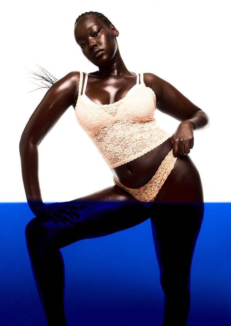 A sultry studio shot of a dark-skinned model in lingerie against a split white and blue background, showcasing fashion and beauty.