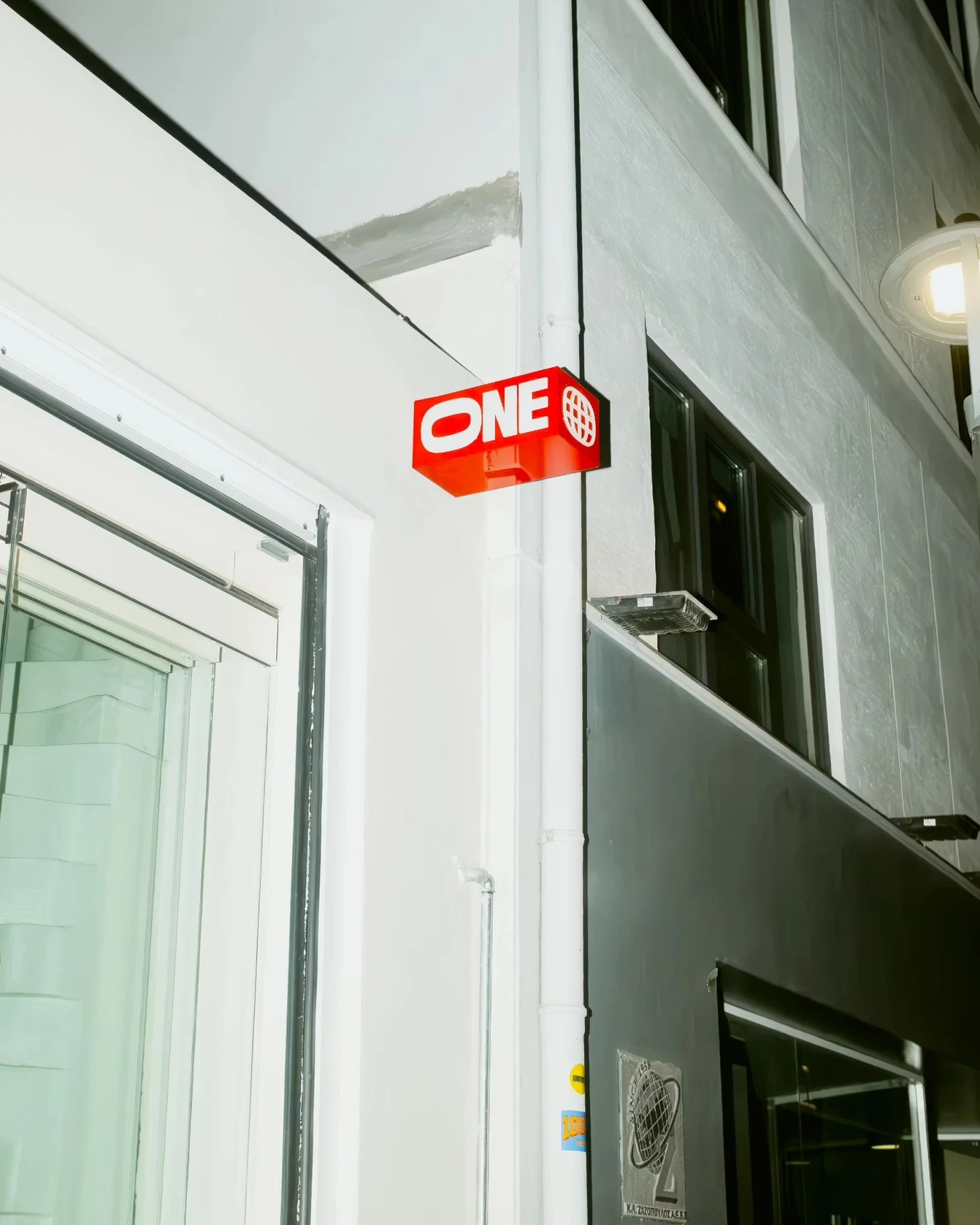 Illuminated red sign with white 'ONE' lettering on a white and grey building, lit by a streetlight, captured at eye-level.
