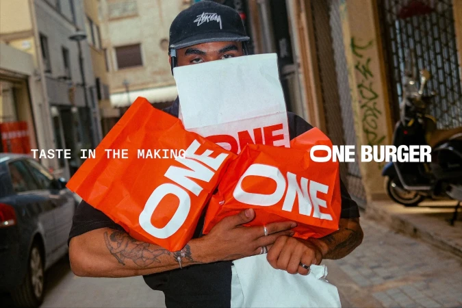 Man holding multiple branded orange and white take-out bags on an urban street.