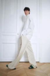 Model walking in a white shirt and cream trousers against white panelled doors