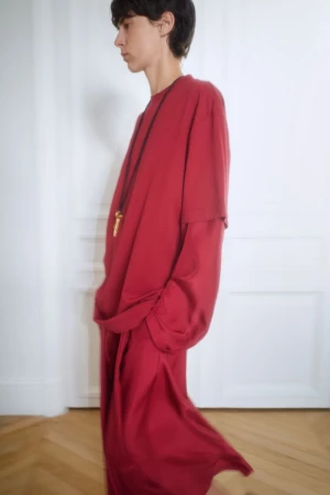 Model wearing a loose red t-shirt and matching trousers with a long dark cord necklace standing indoors