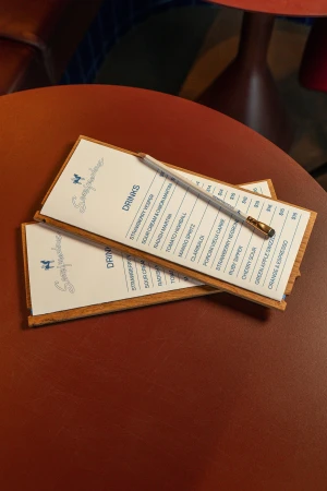Close-up of two restaurant menus with a pen on a brown table, showcasing drink options and prices in a warm-toned setting.