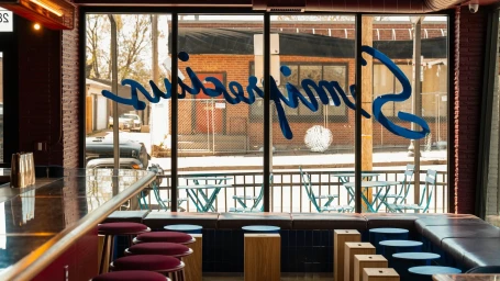 Interior view of Semiprecious restaurant showing bar seating, blue window lettering, and outdoor patio tables.