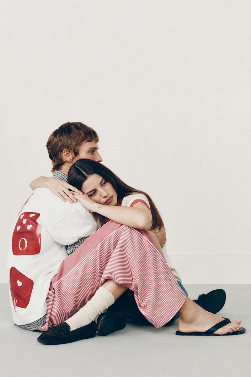 A fashionable couple sitting together on the floor. The woman is leaning against the man with her eyes closed in a brightly lit indoor space.