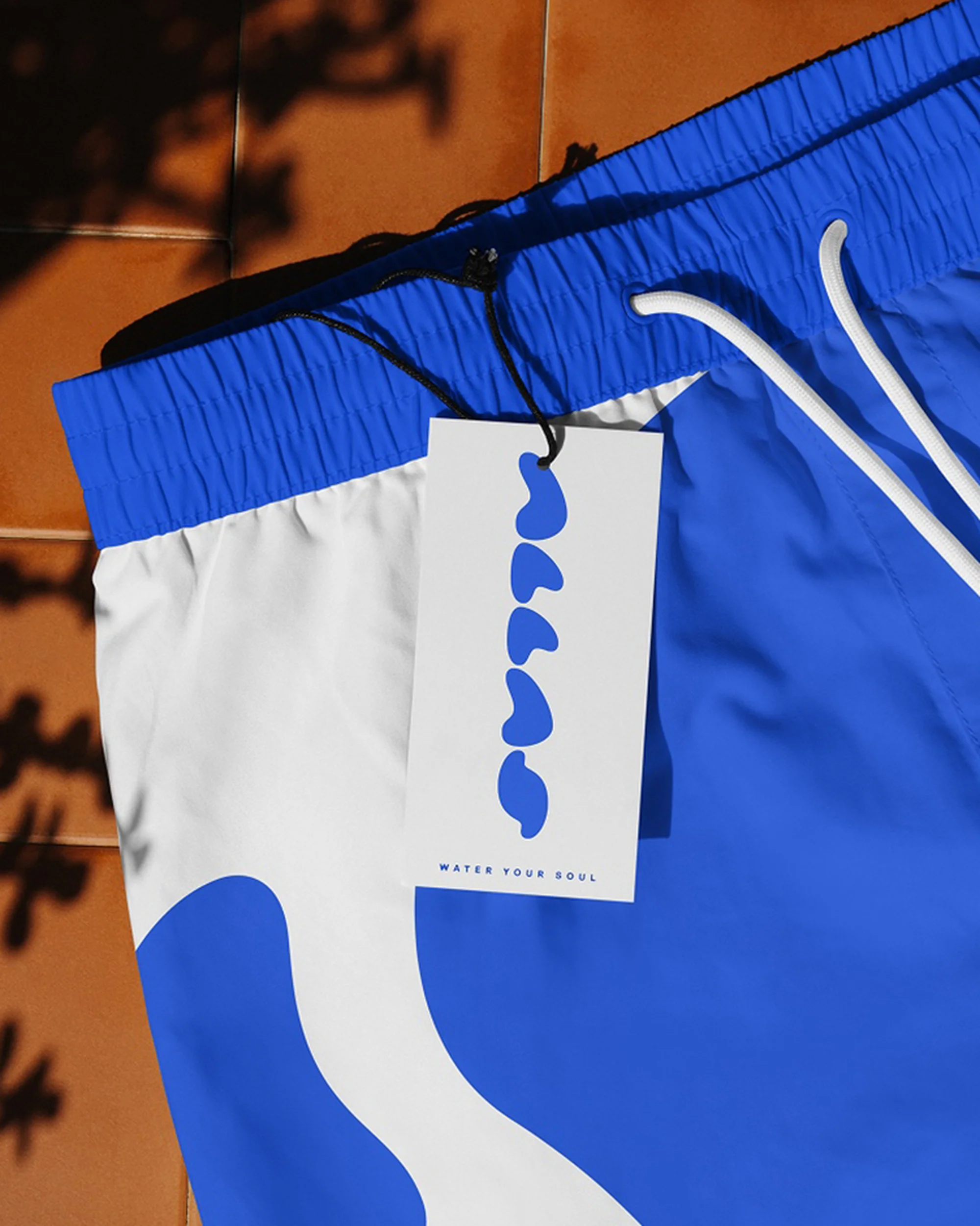 Stylish blue and white swim trunks featuring a unique design and a tag with the text 'Water Your Soul', set on a terracotta tile surface.