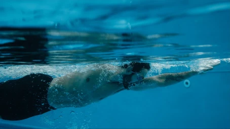 Man swimming underwater in a blue pool wearing dark swimming trunks and goggles during a Brand Identity project for Allas Pool