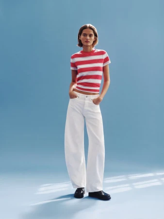 Model wearing a red and white striped t-shirt and wide-leg white jeans against a blue background for Tommy Jeans.