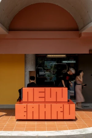Outdoor shot of the Neun Bahru coffee shop seating area with orange block-letter text, patrons, and architectural details in daylight.