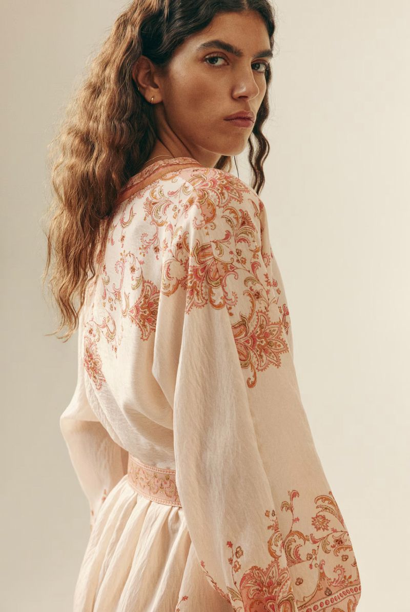 Portrait of a woman wearing a light dress with floral patterns, facing slightly to the left, showcasing fashion and style indoors.