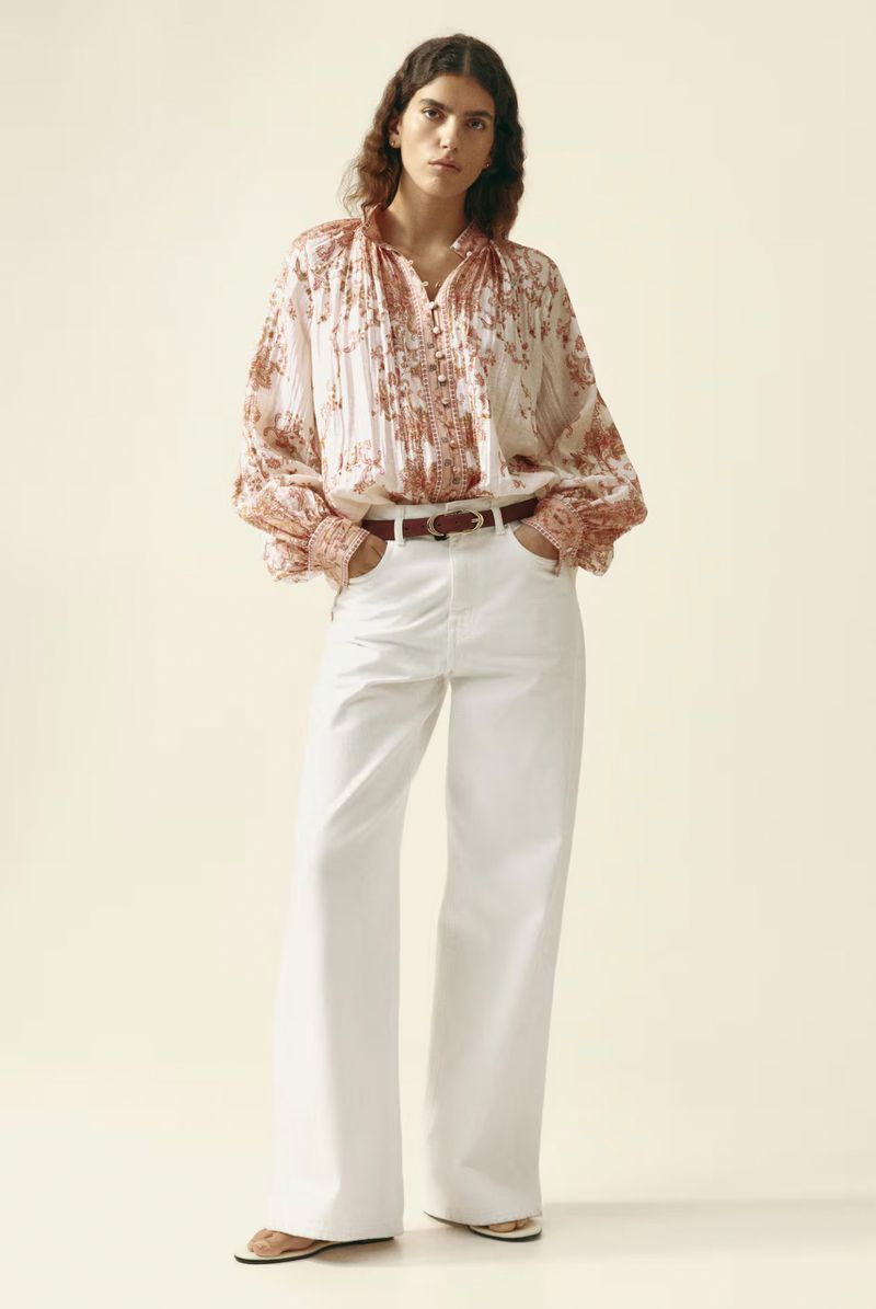 Model in printed patterned blouse and white wide-leg trousers against a seamless pale background