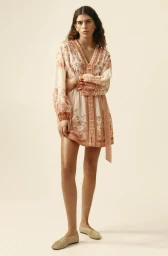 Model standing against a plain background wearing a patterned mini dress and flat woven shoes.