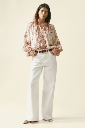 Model in printed patterned blouse and white wide-leg trousers against a seamless pale background