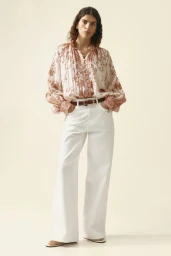 Model in printed patterned blouse and white wide-leg trousers against a seamless pale background