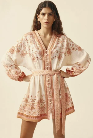 Model wearing a printed V-neck belted tunic dress standing against a plain light neutral backdrop.