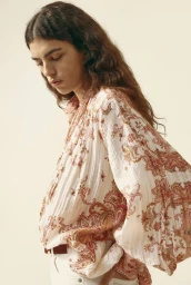Model with long dark wavy hair wearing a printed patterned blouse against a plain light background for H&M.