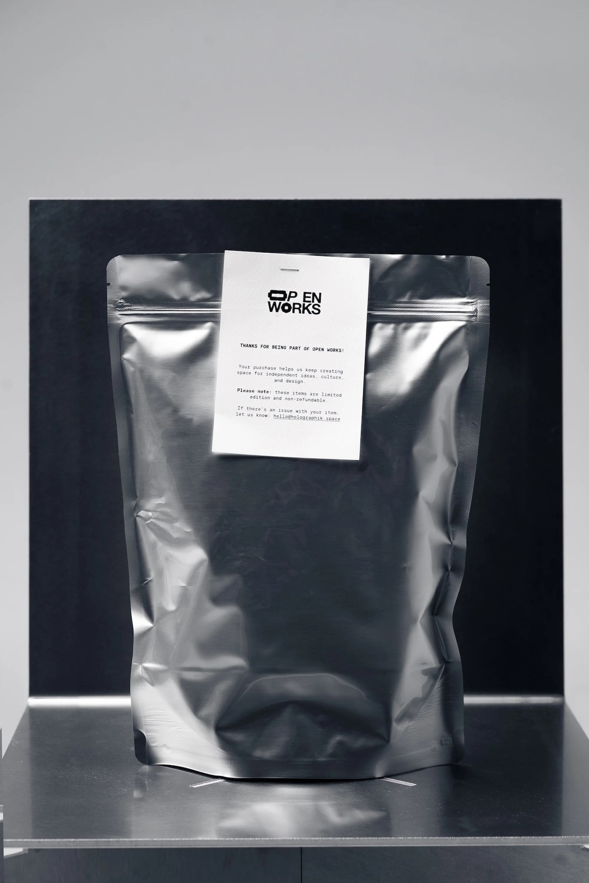 Silver foil package featuring a label for Open Works, set against a minimalist studio background, highlighting product presentation.