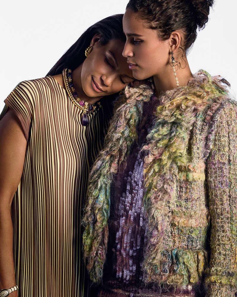 Two women in stylish outfits pose in a fashion shot against a white backdrop, one with a striped top and the other with a colorful jacket.